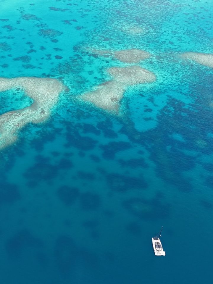 A catamaran at anchor among turquoise reefs, from the air