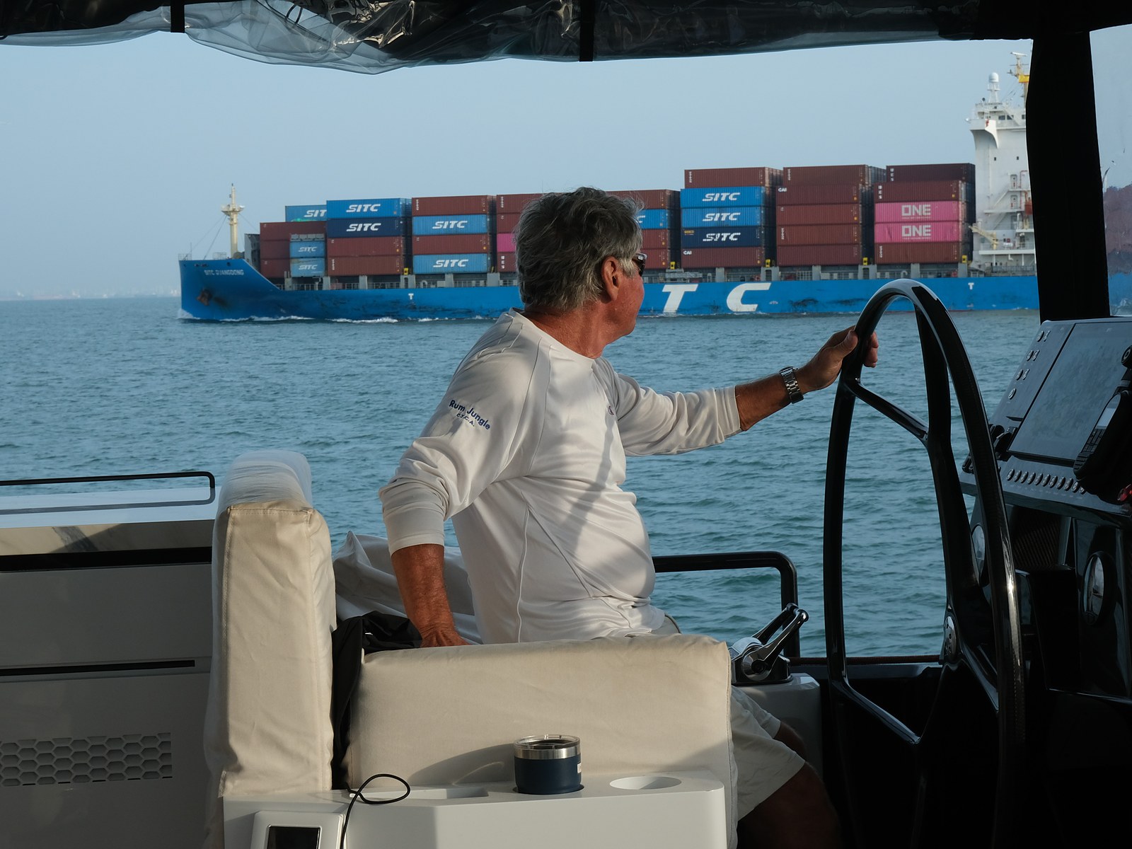At the helm of a catamaran, a container ship crossing astern
